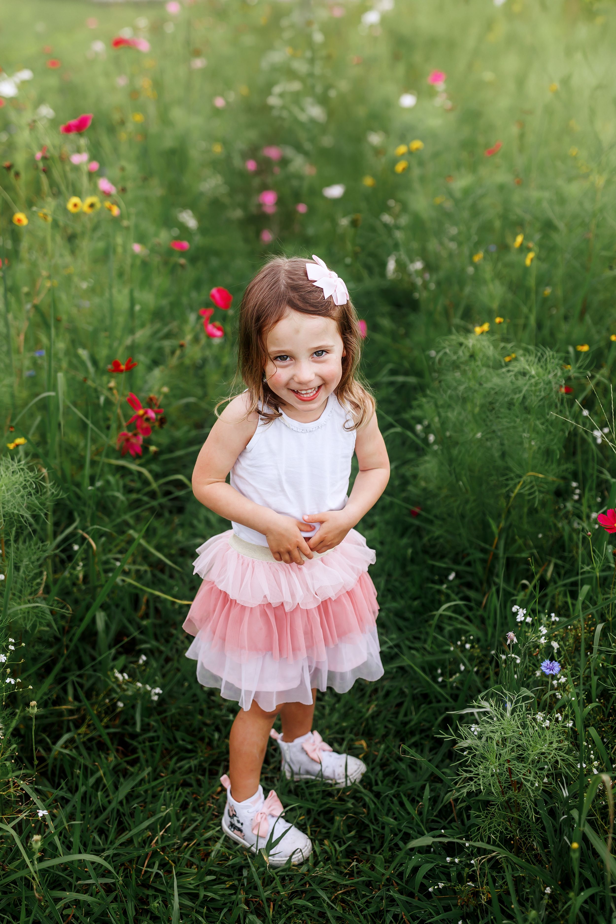 A child in a white top and pink tulle skirt stands in a wildflower meadow with red and yellow blooms.