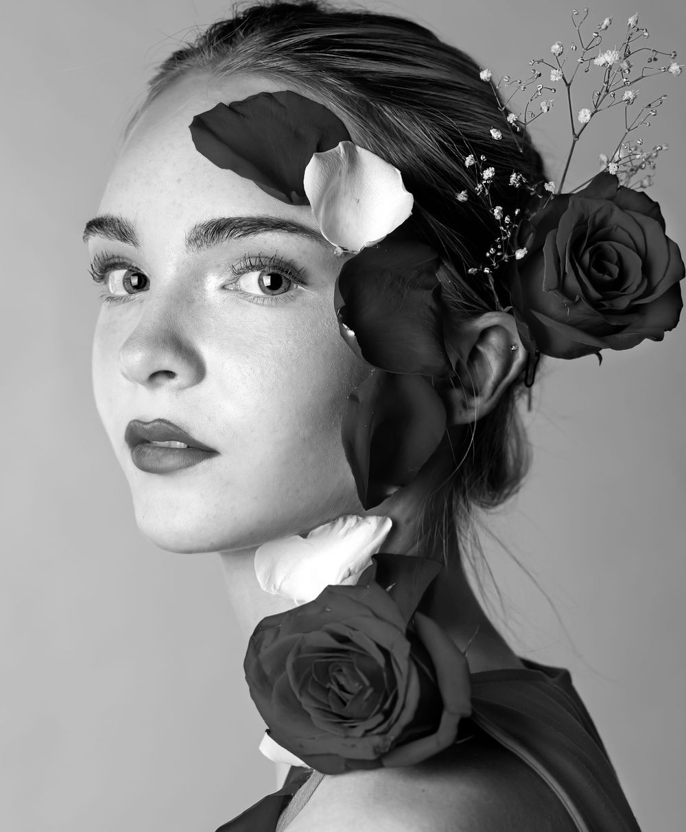 Black and white image of a girl looking at the camera with roses on her face and head