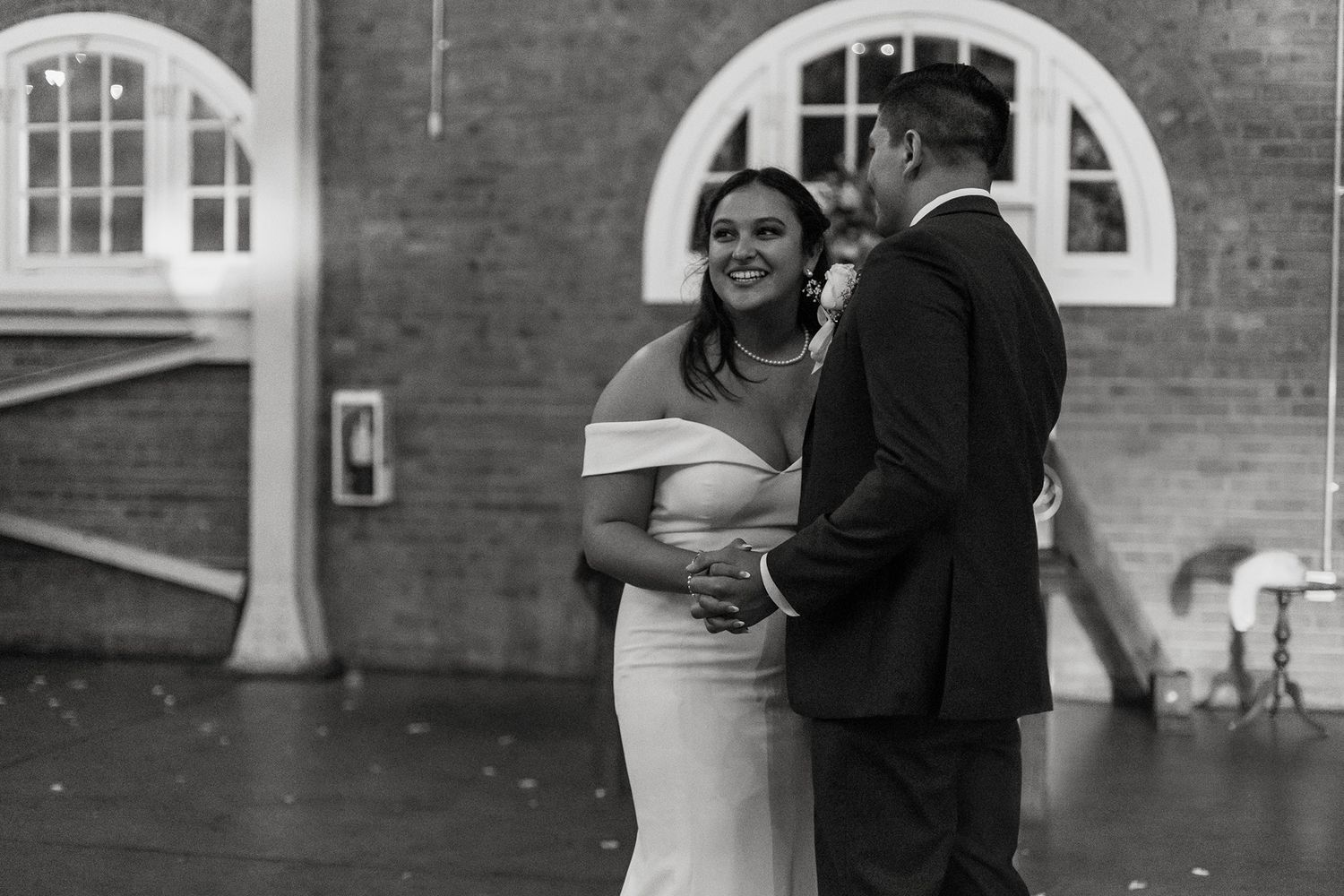 A couple shares their first dance in a room with brick walls with arched windows.