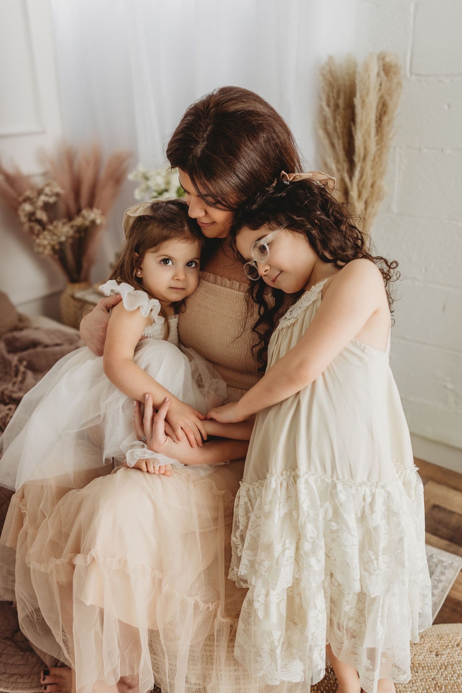 A tender family moment captured in soft beige tones with delicate lace dresses and dried pampas grass decor.