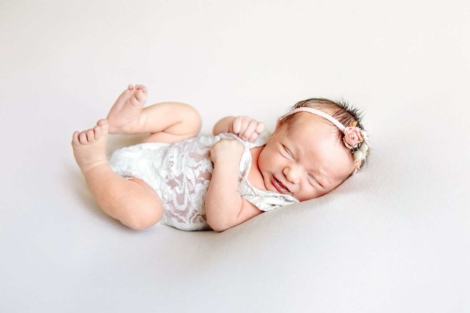 Sleeping newborn baby girl in white lace romper and floral headband on white background.