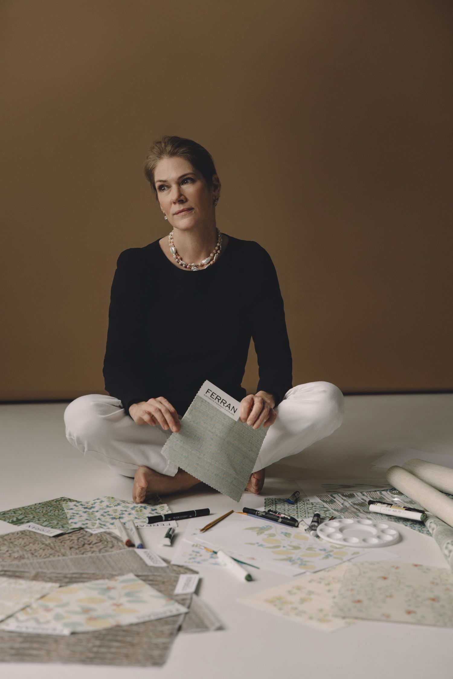 A person in black attire sits at a table reviewing papers and documents spread across a light colored surface.