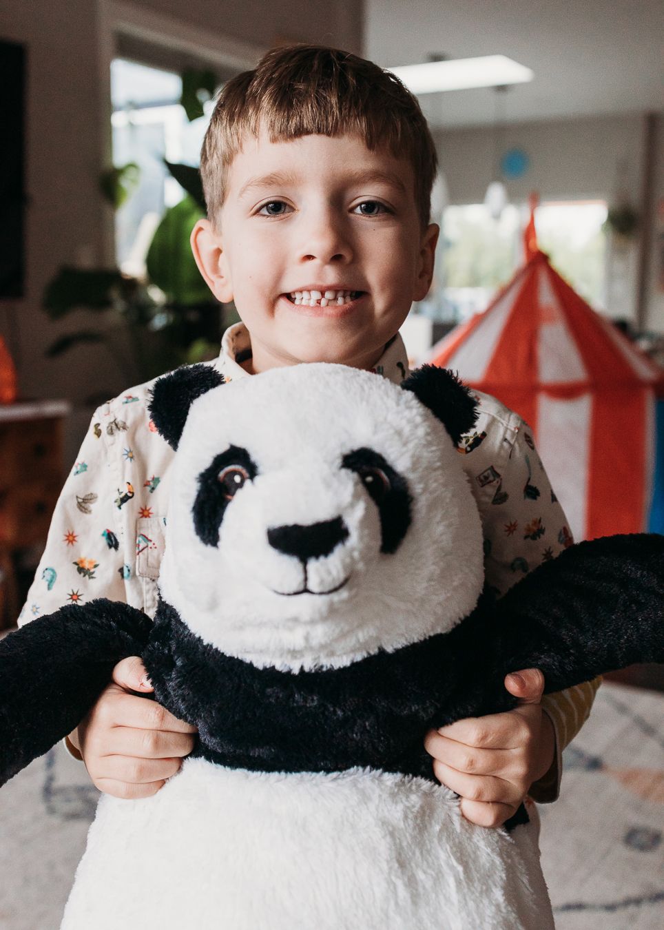 A plush panda toy being held and displayed against a blurred indoor background with red decorations.