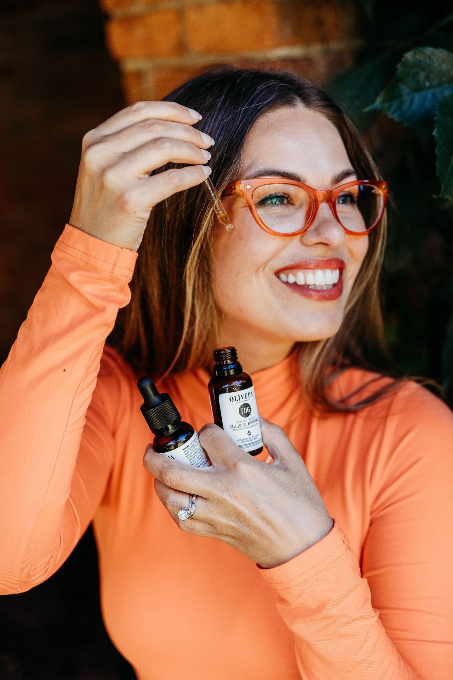 Person in orange turtleneck and patterned skirt poses against brick wall with green ivy leaves.