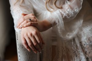 Close-up details of delicate lace and beading on a white wedding dress with hands gently touching the fabric.