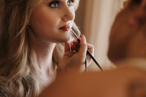 Professional makeup artist applying cosmetics to model in warm natural lighting.