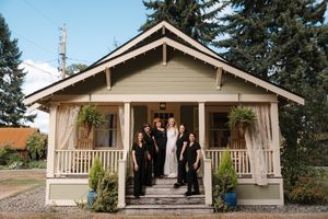 A rustic craftsman-style wedding venue with a covered porch and evergreen trees in the background.
