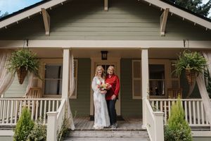 A rustic front porch of a beige house with white trim and hanging plants creates a welcoming entrance.