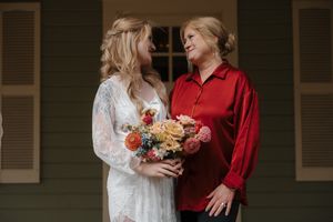 A couple in red and white outfits stands close together while holding flowers during a romantic photoshoot.