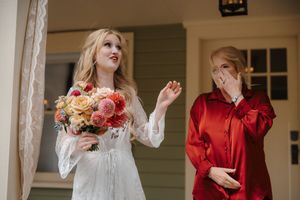 Wedding couple shares a candid moment in front of a white porch wearing contrasting red and white outfits.