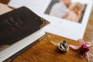 Wedding rings and photography details arranged artistically on a rustic wooden surface with printed materials.