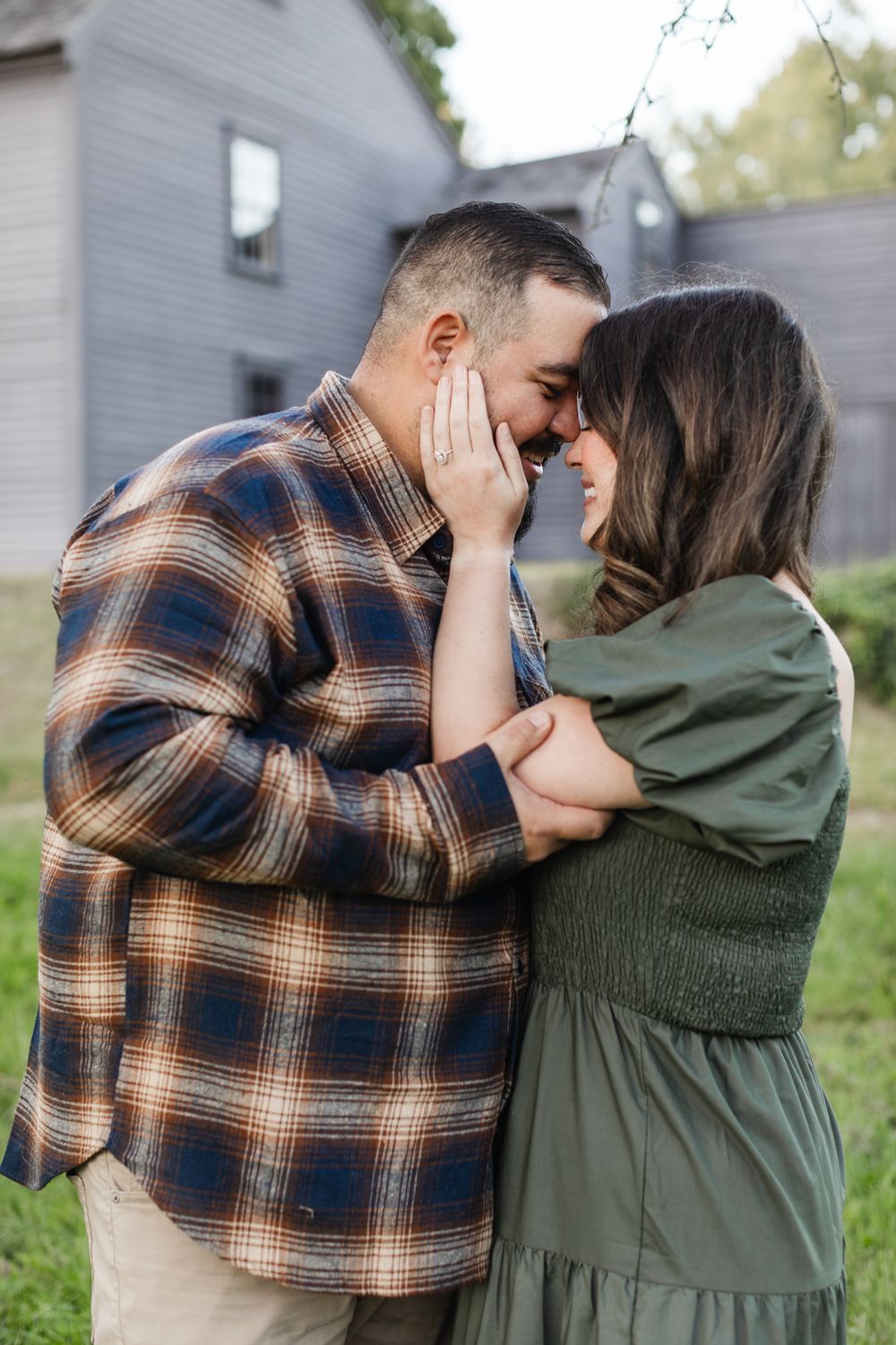 Woman in grey dress holds her fiancee's face to display her new engagement ring for engagement photos in Middlesex County, Massachusetts.