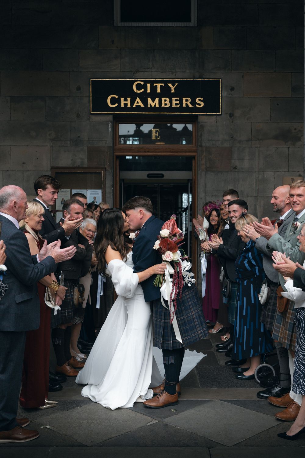 A sequence of wedding photos showing a newlywed couple dipping and kissing while guests line up outside city chambers.