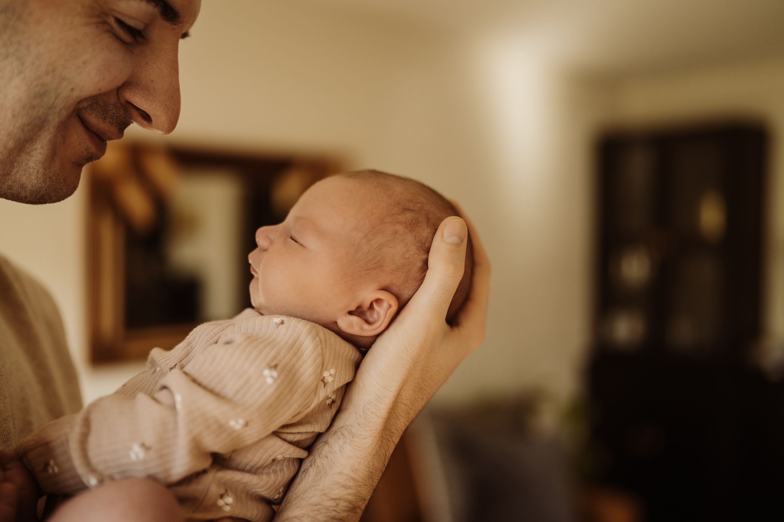 A parent's hands gently hold and comfort a sleeping baby in a warm, intimate indoor setting.
