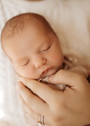 A sleeping newborn baby peacefully resting while being cradled by gentle hands with a ring.