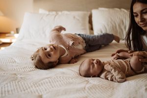 Newborn baby sleeping peacefully on white bedding in warm natural light.