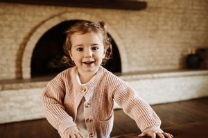 A child in a pink sweater crawls and plays on a hardwood floor in a vintage-toned photograph.