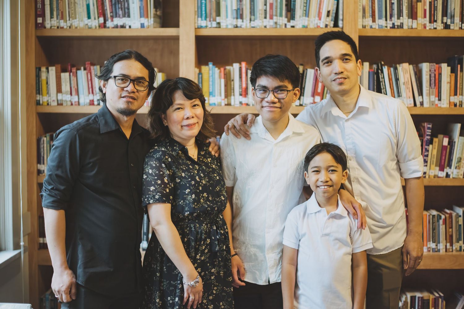 A family of six poses together outdoors in formal attire with blooming white flowers in the background.