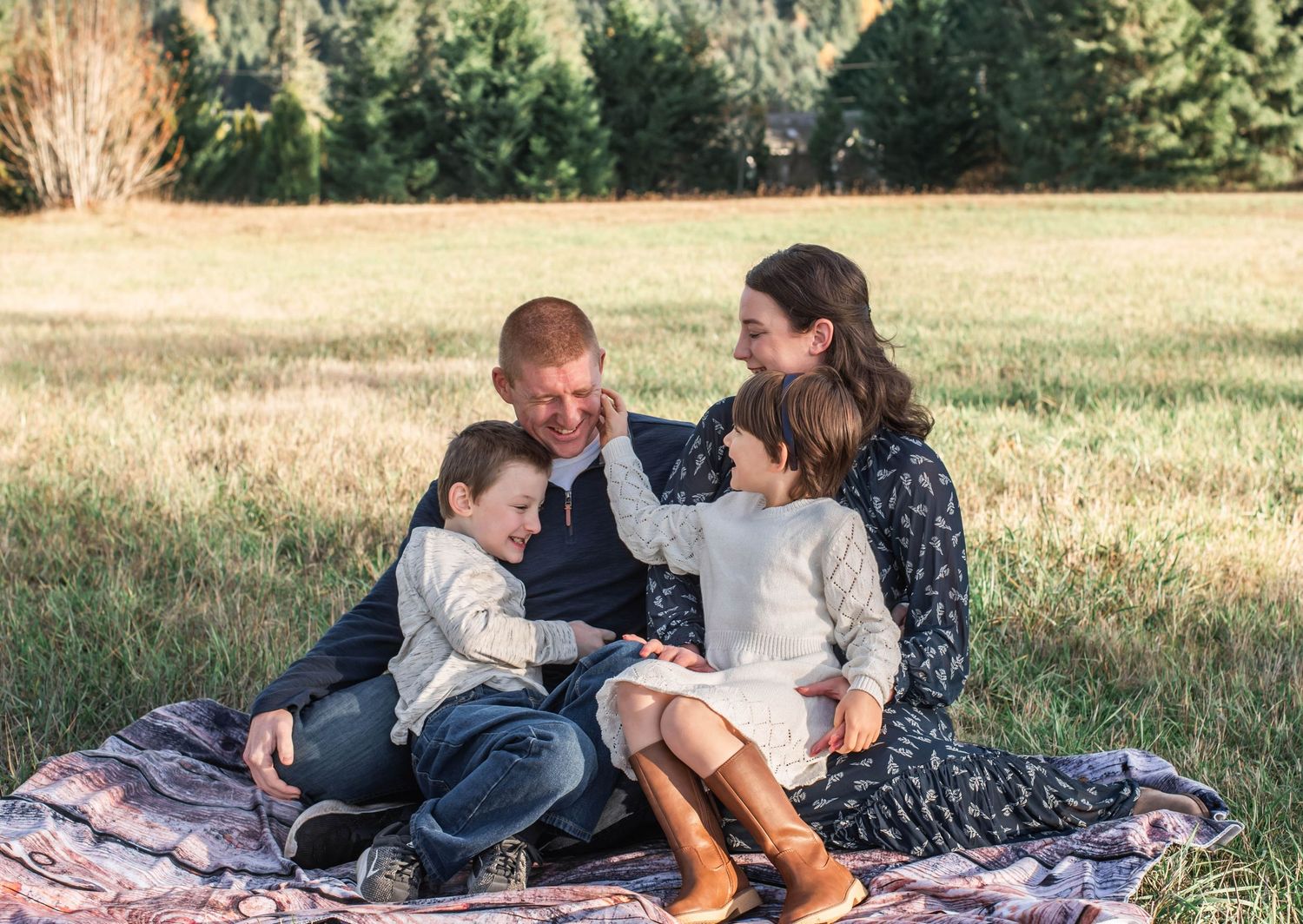 A family sits together on a picnic blanket in a grassy field during golden hour.
