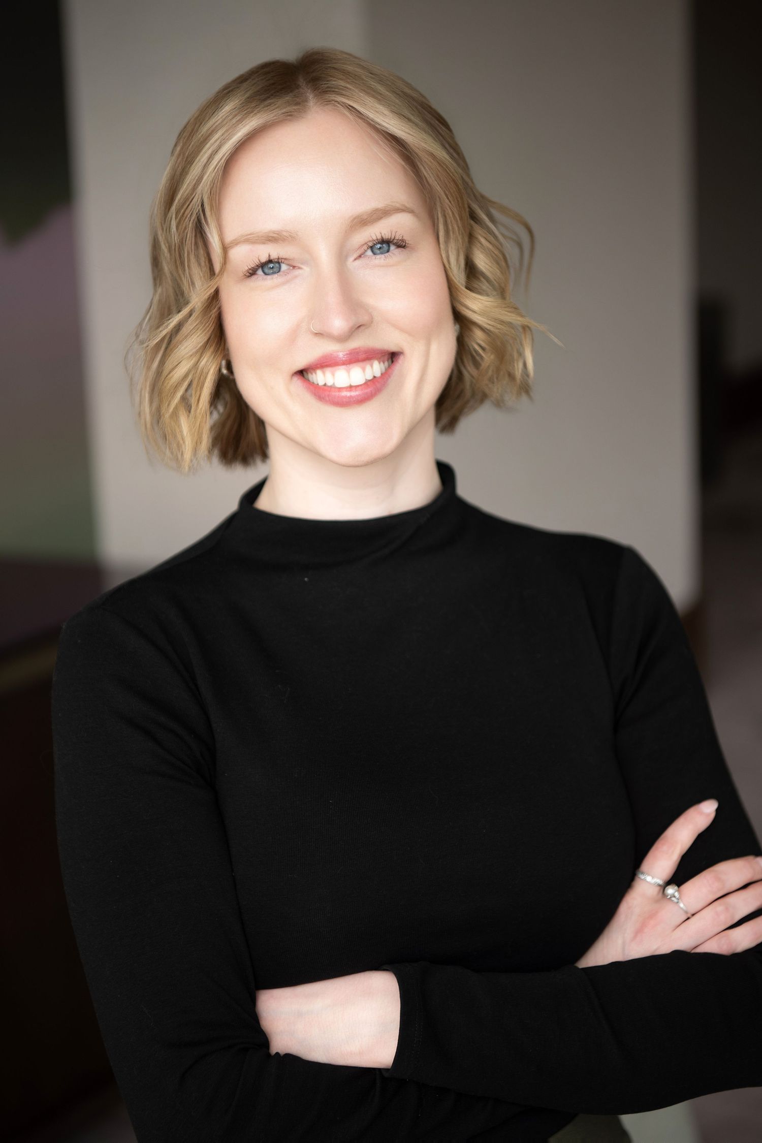 Professional wearing navy blazer and black top sits casually in office setting with warm lighting.