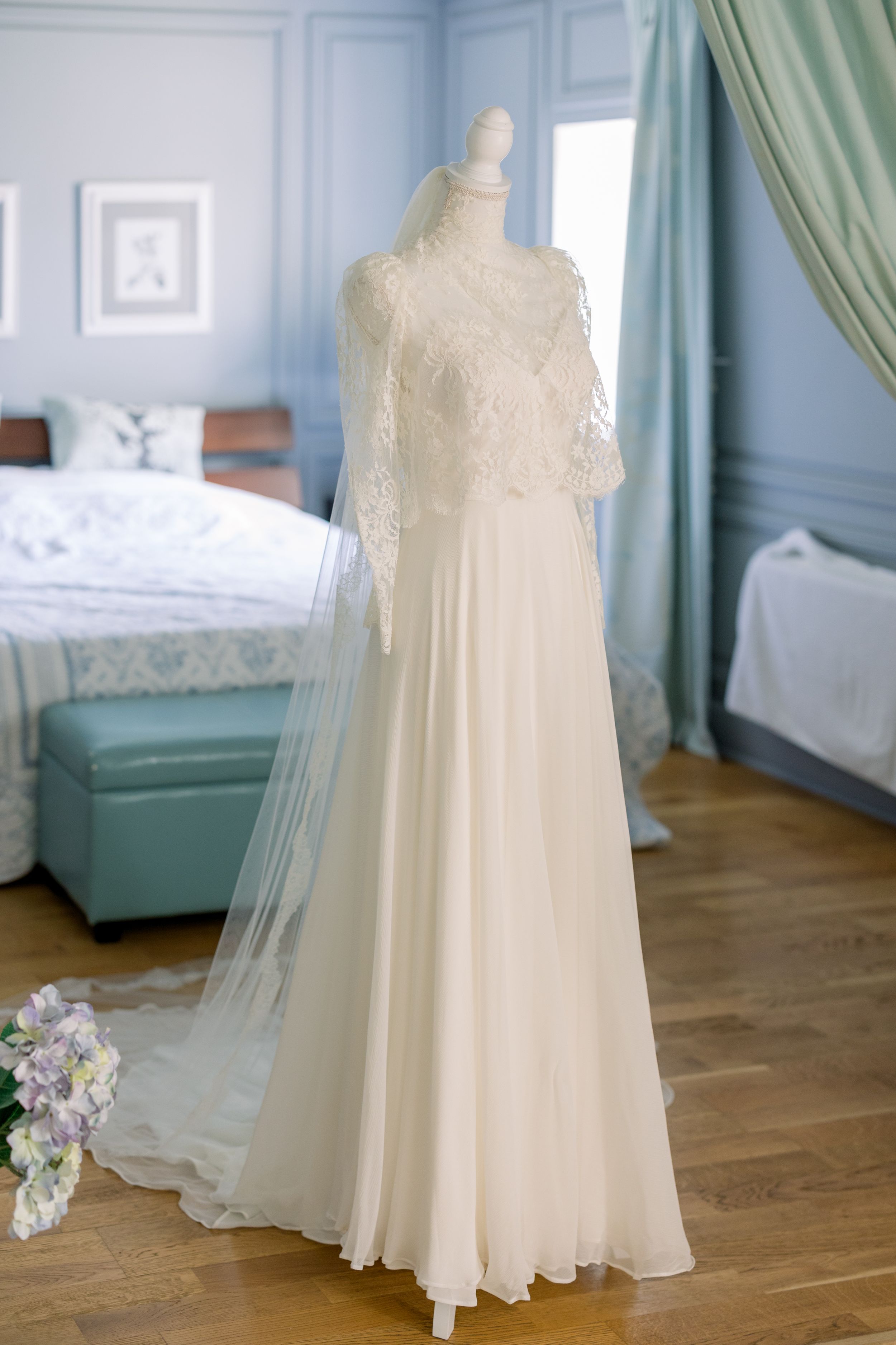 An elegant lace wedding dress with sheer sleeves displayed on a mannequin in a blue room.