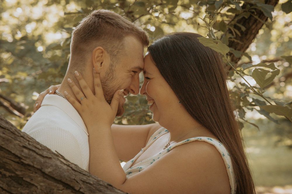 A couple shares an intimate romantic moment outdoors leaning against a tree in warm golden lighting.