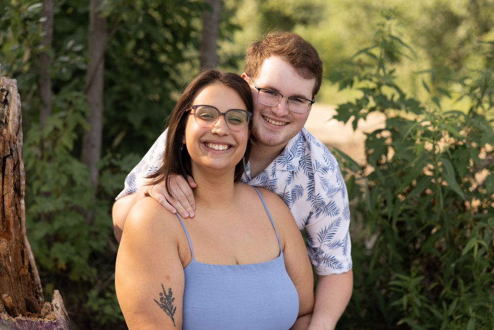 A couple embraces outdoors in a garden setting during a sunny portrait session.