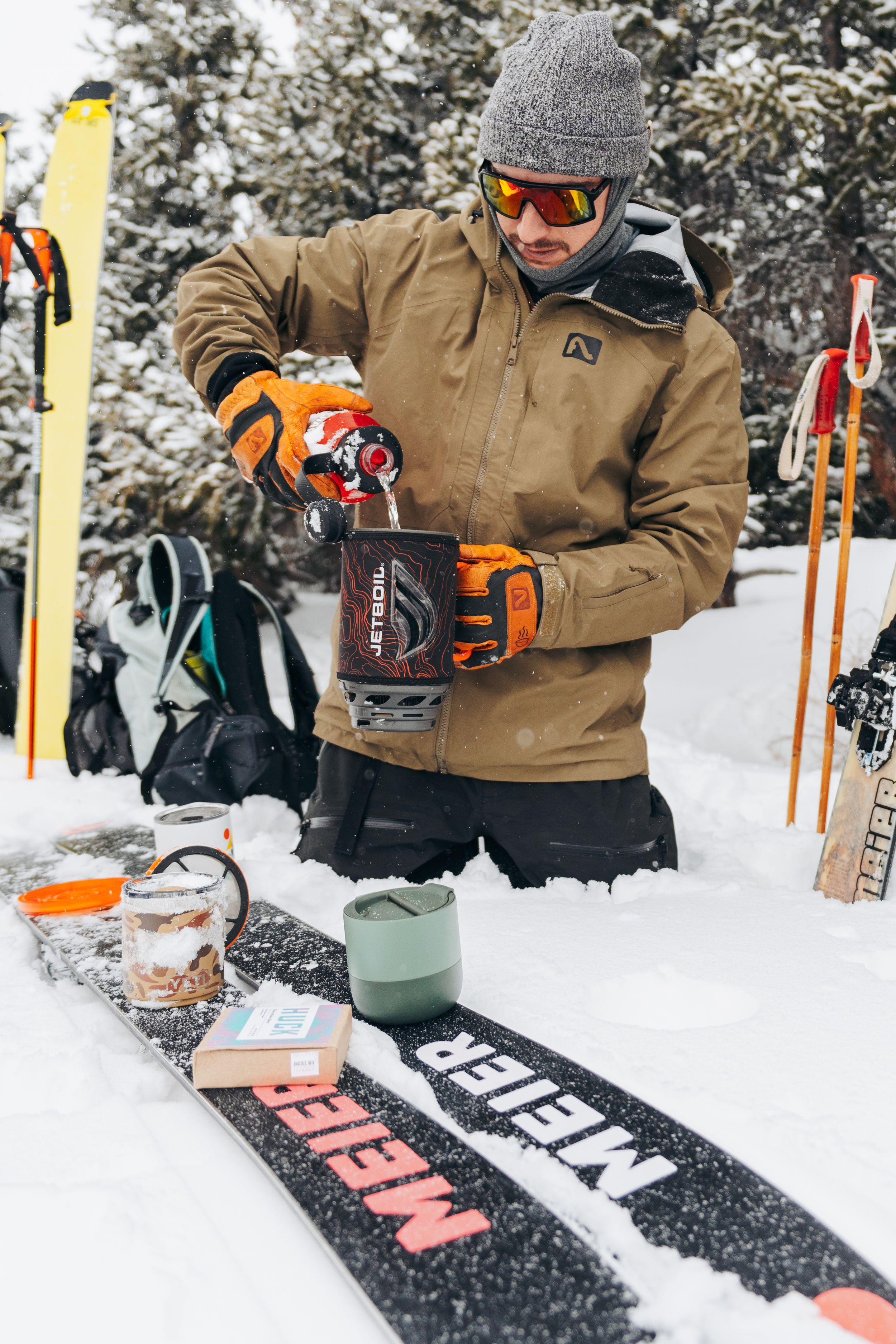 Skier waxing and maintaining their skis in snowy winter conditions with orange tools and equipment.
