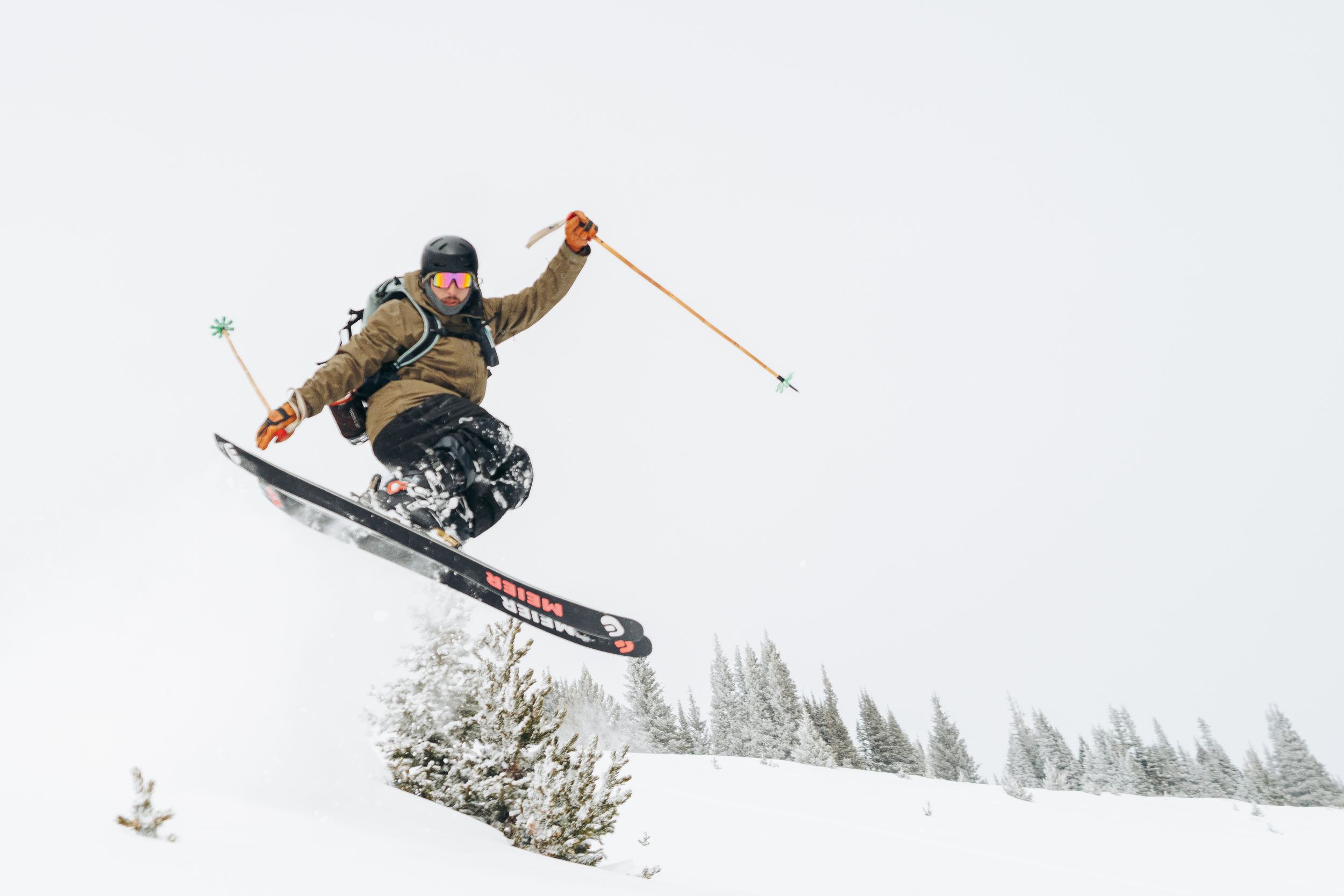 Snowboarder performs aerial trick against snowy mountain backdrop while jumping off snow ramp.