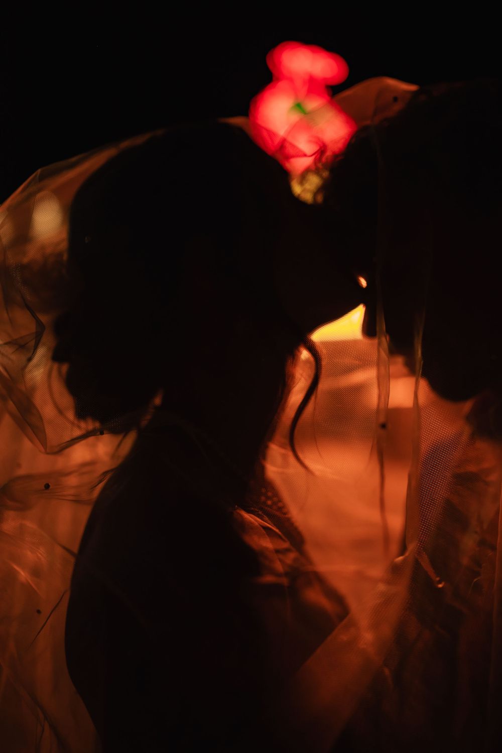 A dark silhouetted couple embraces under warm red lighting creating a romantic nighttime atmosphere.