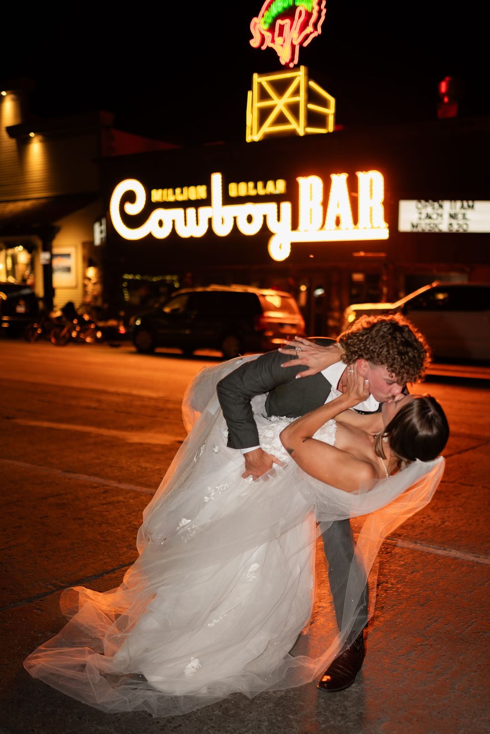 A romantic dip pose at night in front of an illuminated theater with a flowing white wedding dress.