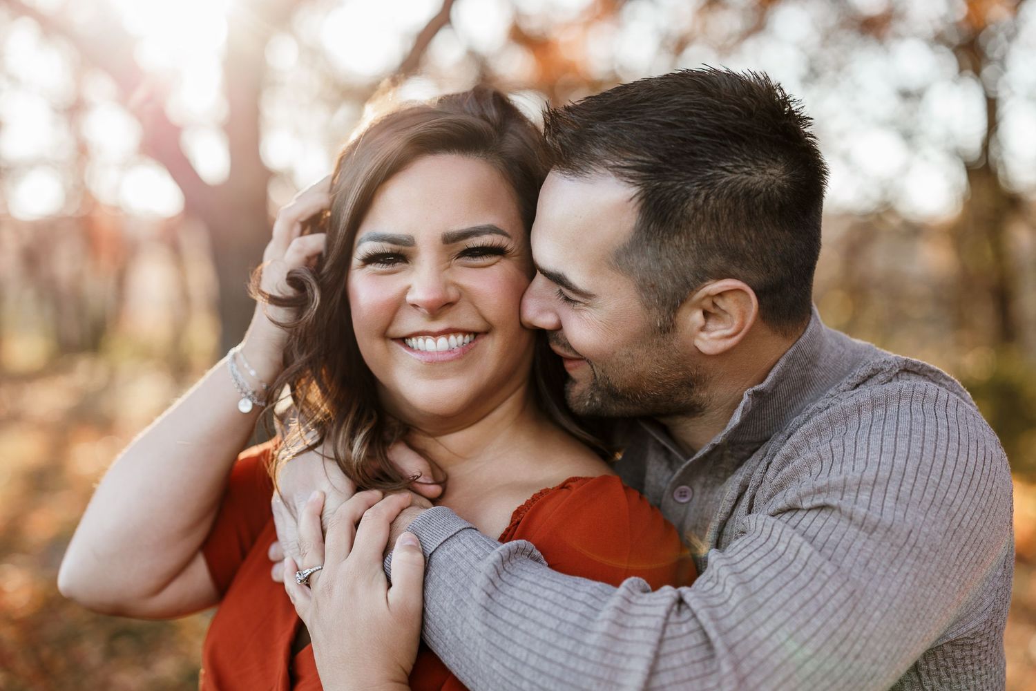 A couple embraces and laughs together during a romantic outdoor photoshoot in warm autumn lighting.