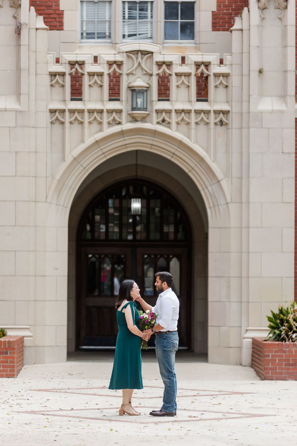A couple stands in front of an ornate stone archway with Gothic architectural details during a special moment.