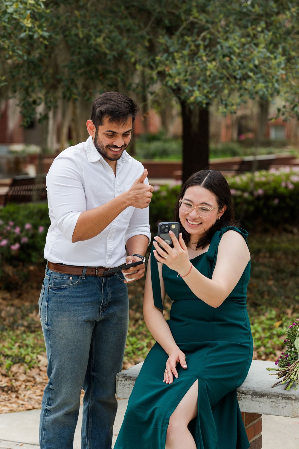 Two people laughing while looking at their phones in front of a red brick building.