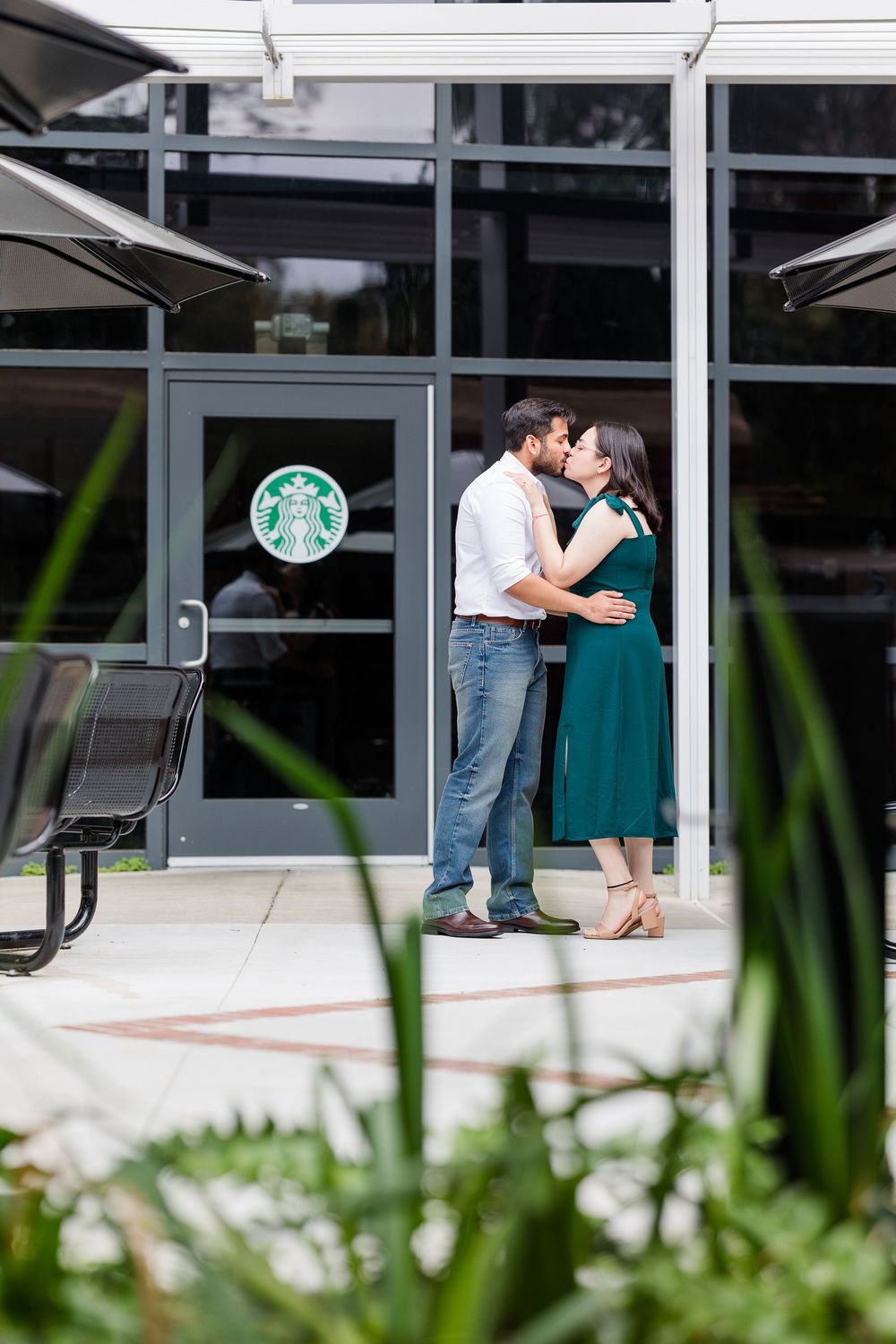 A couple shares an intimate moment outside a modern building with glass windows and a Starbucks sign visible.