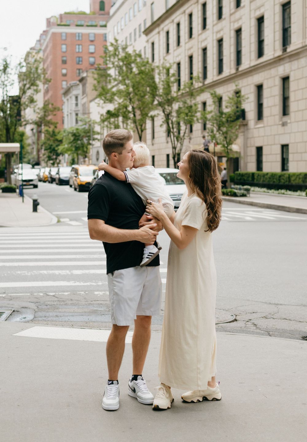 A couple shares a tender moment on a tree-lined street corner in an upscale urban neighborhood.