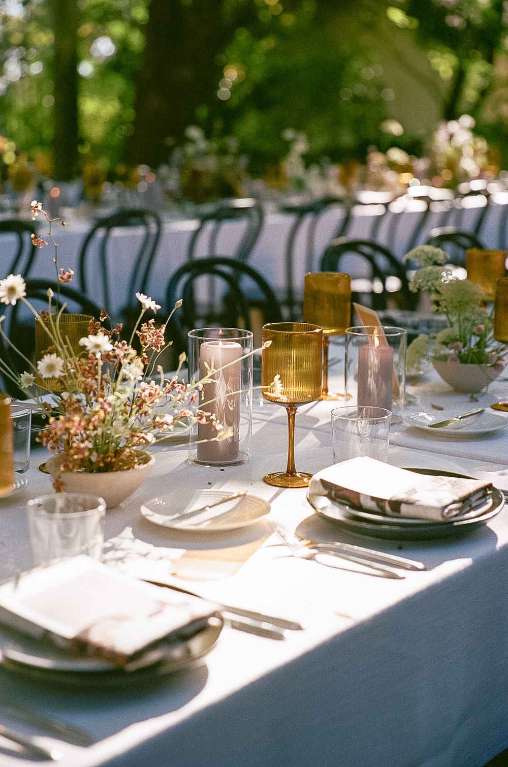 Elegant outdoor table setting with amber wine glasses, white linens, and delicate floral centerpieces for a garden wedding reception.