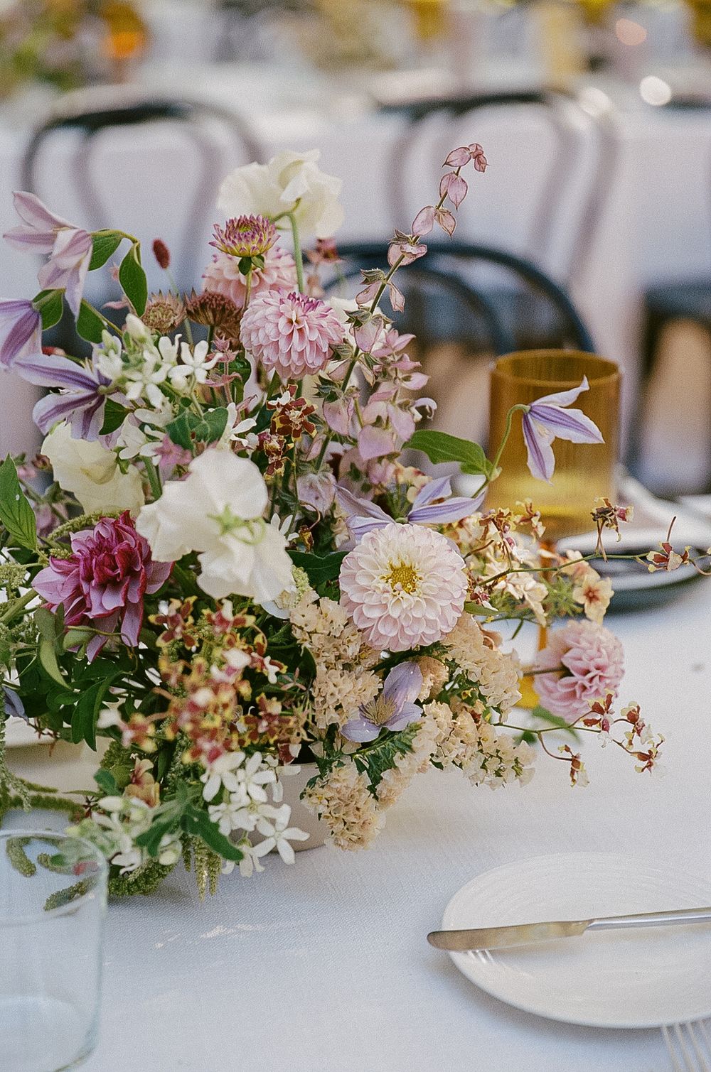 Elegant floral centerpiece with pink dahlias, white flowers and delicate greenery on a wedding reception table setting.