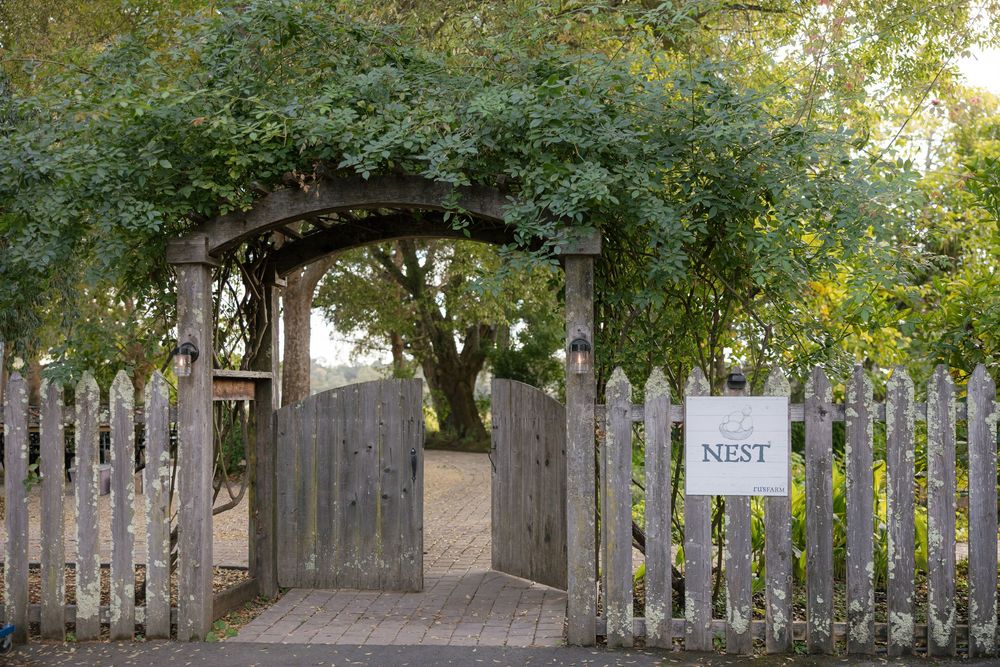 A rustic wooden garden gate with an arbor covered in green foliage leads to a garden path.
