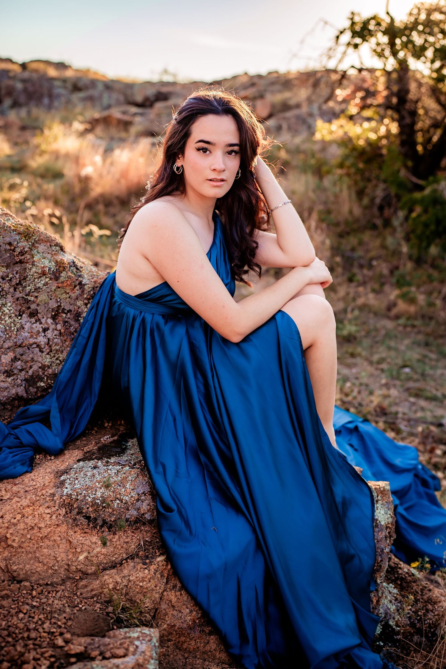 A flowing royal blue dress contrasts beautifully against rocky terrain during golden hour sunset lighting.