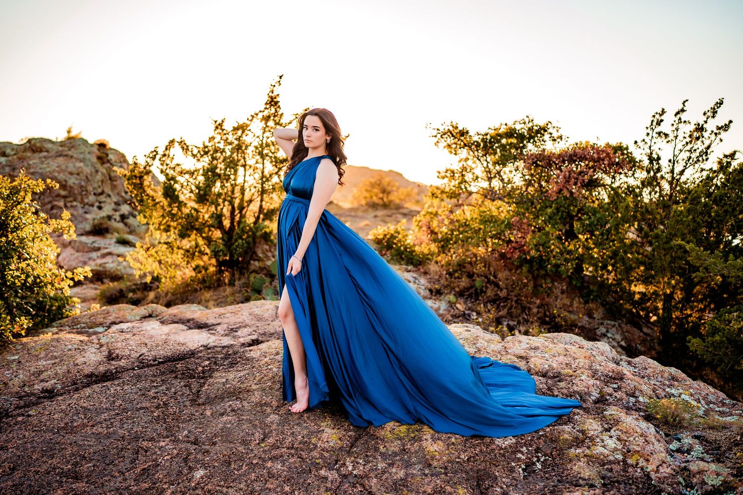 A flowing royal blue dress billows dramatically against a desert landscape at sunset.