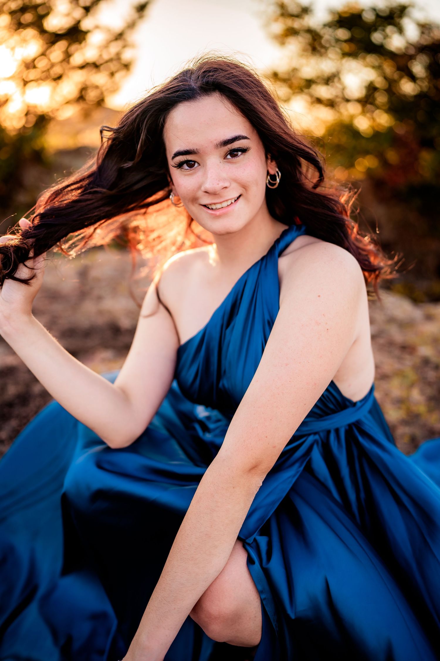 A person in a navy blue dress poses outdoors during golden hour sunset with dramatic lighting and shadows.