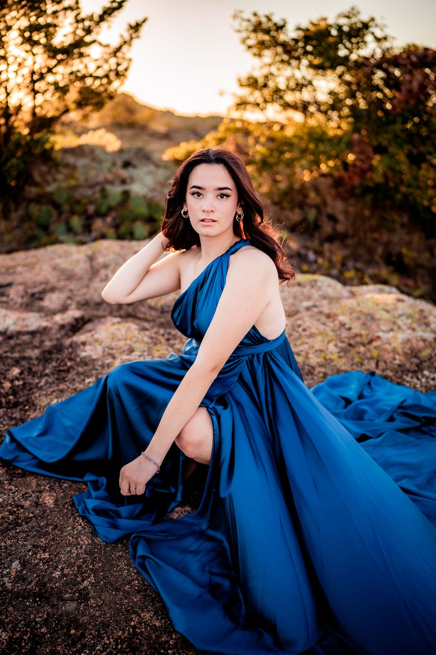 A flowing royal blue dress creates dramatic contrast against rocky desert terrain at golden hour sunset.