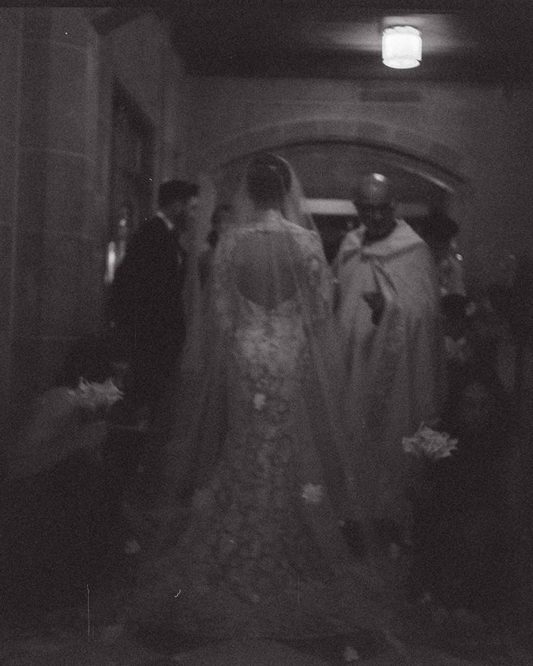 A dark and grainy black and white photograph shows several figures walking through a dimly lit corridor.