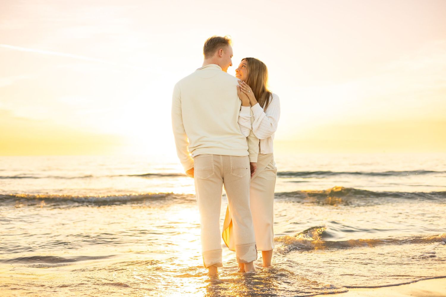 Couple sharing a romantic sunset moment on a beach, standing in shallow waves with golden light behind them at Lido key beach