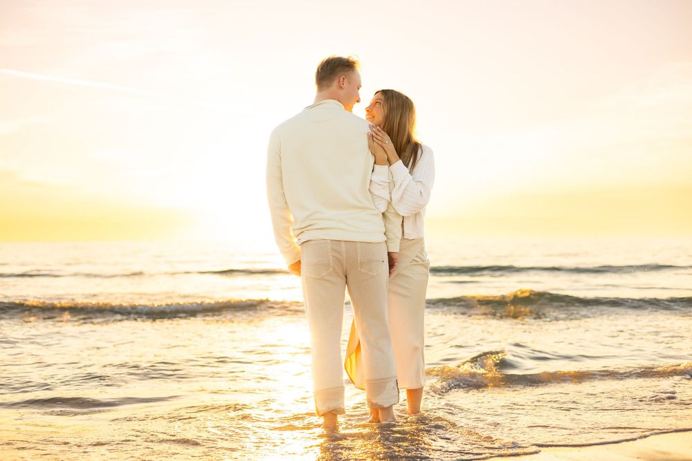 Couple sharing a romantic sunset moment on a beach, standing in shallow waves with golden light behind them at Lido key beach