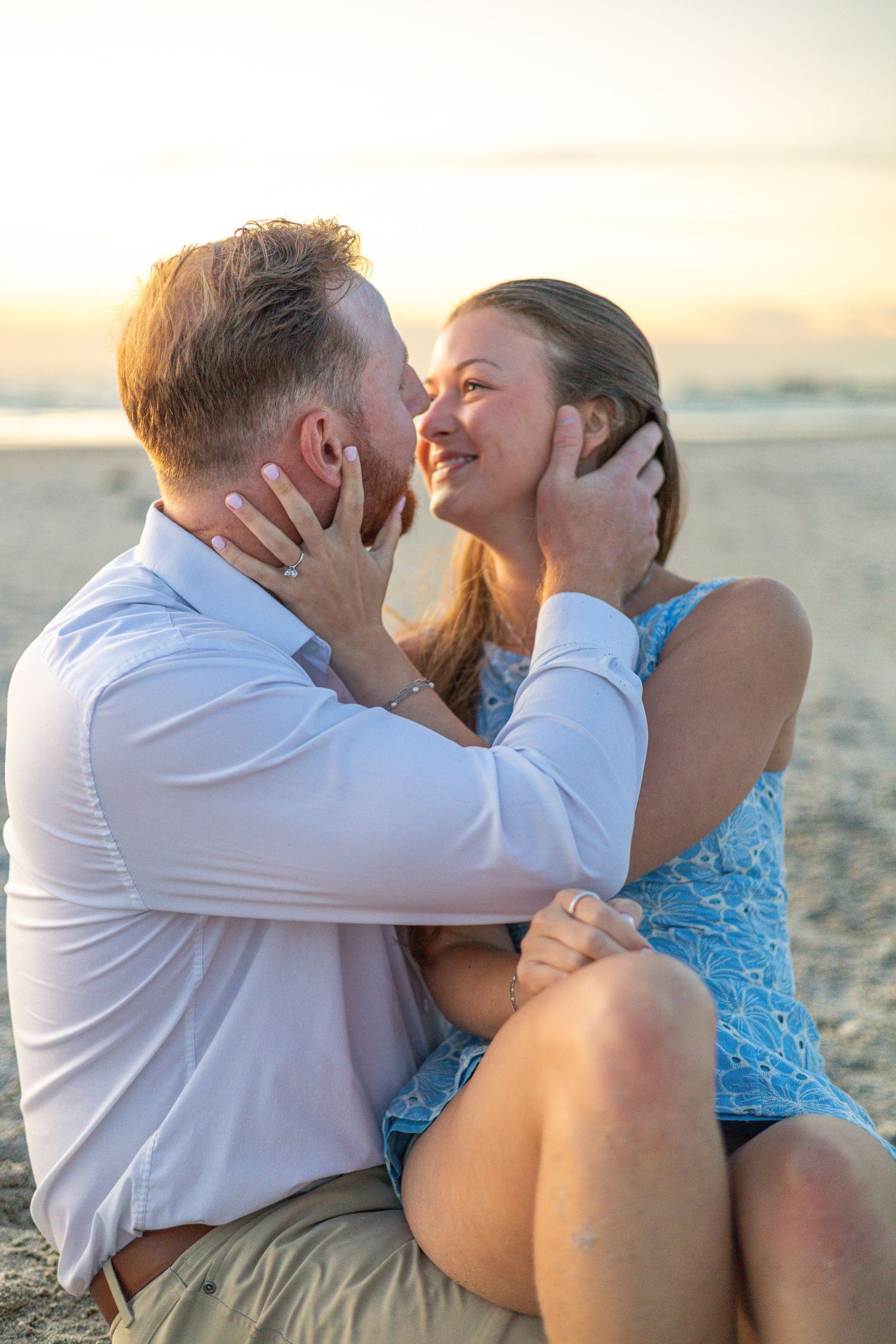 Couple sharing a romantic moment on the beach at sunset, sitting in sand while tenderly holding each other's faces. Lido Beach FLorida