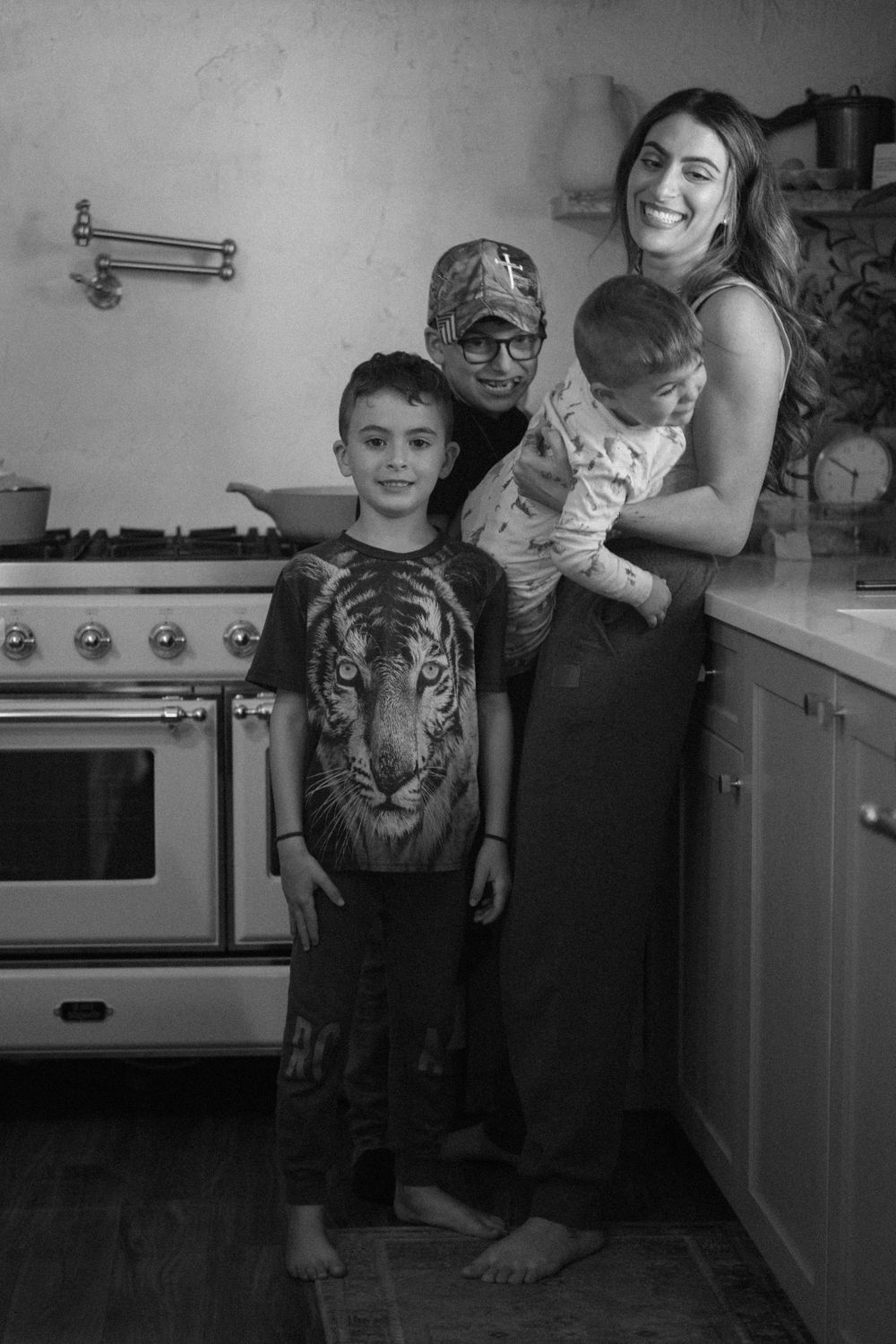 Black and white photo of a smiling family with two boys and a woman posing together in a cozy kitchen.