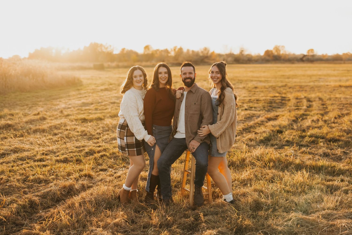 Group of people sitting together in a golden field at sunset creating a warm and intimate outdoor portrait session.