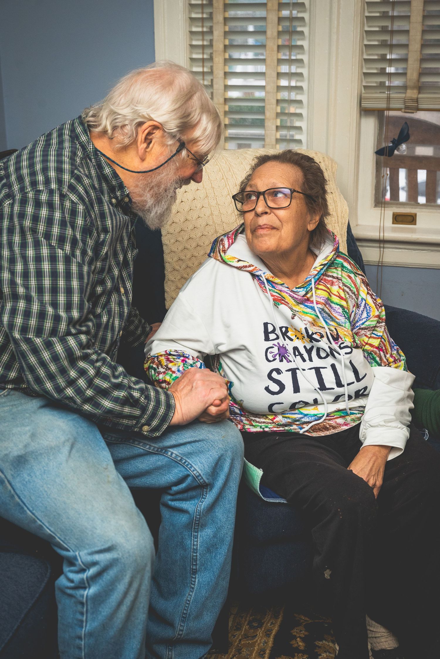 An elderly couple sitting together and interacting affectionately in a cozy indoor setting.